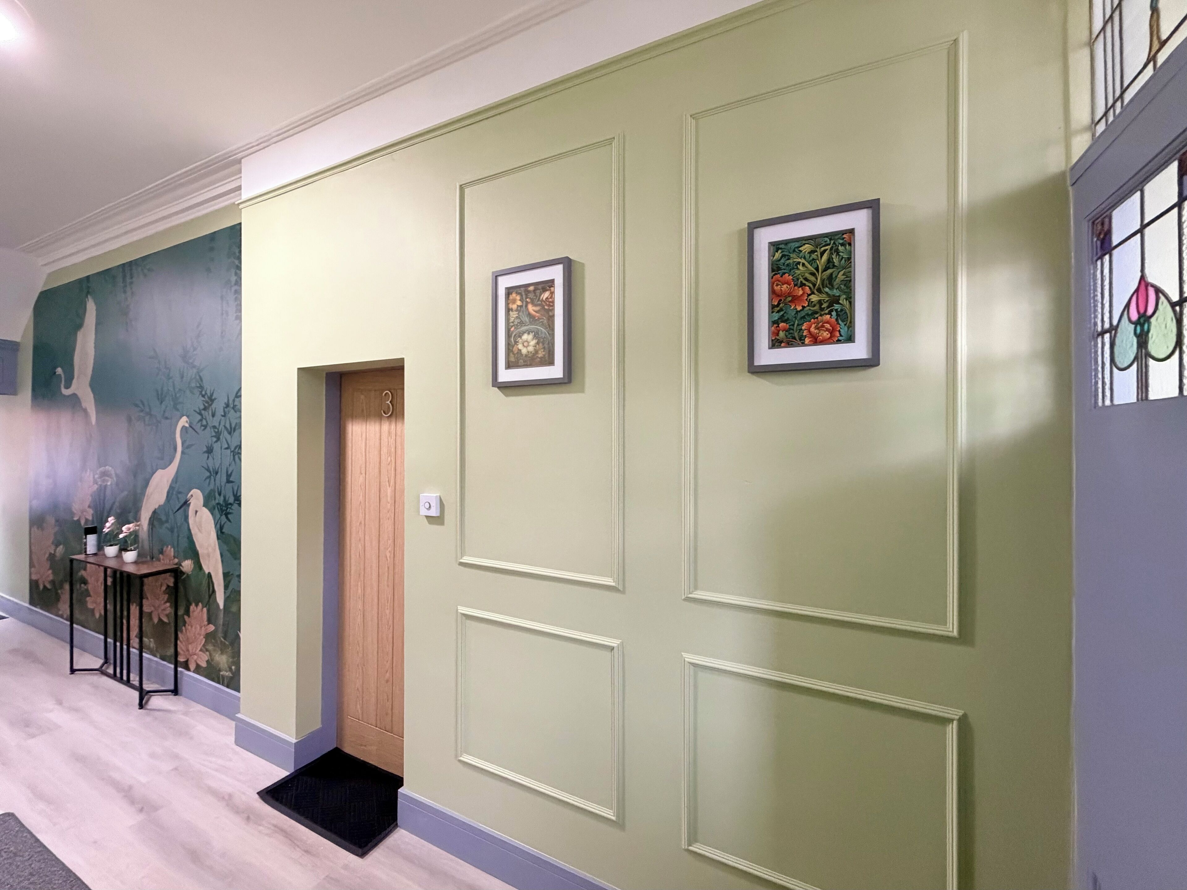 Um corredor com paredes verdes, uma porta de madeira com a inscrição '3' e duas molduras.