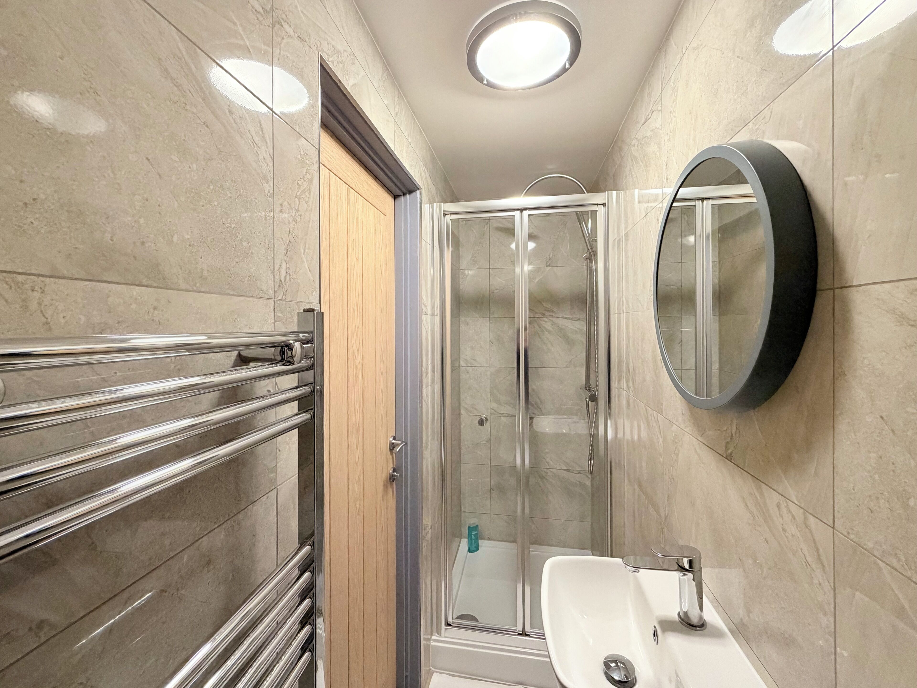 Een moderne badkamer met een douchecabine van glas, een witte wastafel en een ronde spiegel.