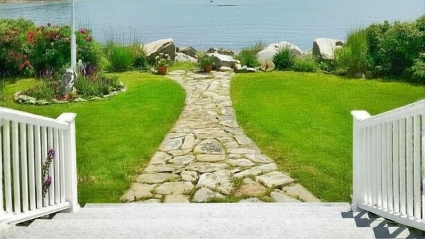Un camino de piedra que lleva a una vista del mar, con una bandera estadounidense, puertas blancas y un cielo despejado.