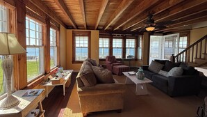 Un salón amplio con vigas de madera, ventanas grandes, un sofá, un sillón y una mesa.