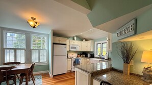 Una cocina con armarios blancos, encimera de granito, refrigerador y microondas.