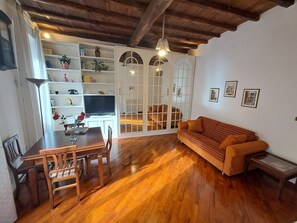 A living room with a wooden floor, a sofa, a dining table with chairs, a TV, and a bookshelf. - Home Piazza Dell'Orologio (Rome)