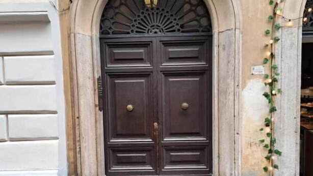Une porte à deux battants en bois foncé, surmontée d’une arche décorative et d’une petite enseigne.