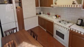 Une cuisine compacte avec des meubles en bois, un réfrigérateur blanc, une cuisinière et une table à manger avec des chaises.