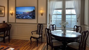 Een eetruimte met een ronde tafel, stoelen, een aan de muur bevestigde televisie en een raam met gordijnen.
