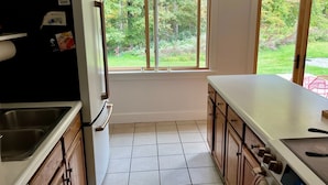 A kitchen with a window, white cabinets, a stainless steel sink, and a stove. - Charming Berkshire Bungalow: Deck, Firepit, Stargazing (Egremont)