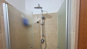 Una ducha a ras de suelo con cabezal de ducha de mano, grifo de pared y desagüe en el suelo.