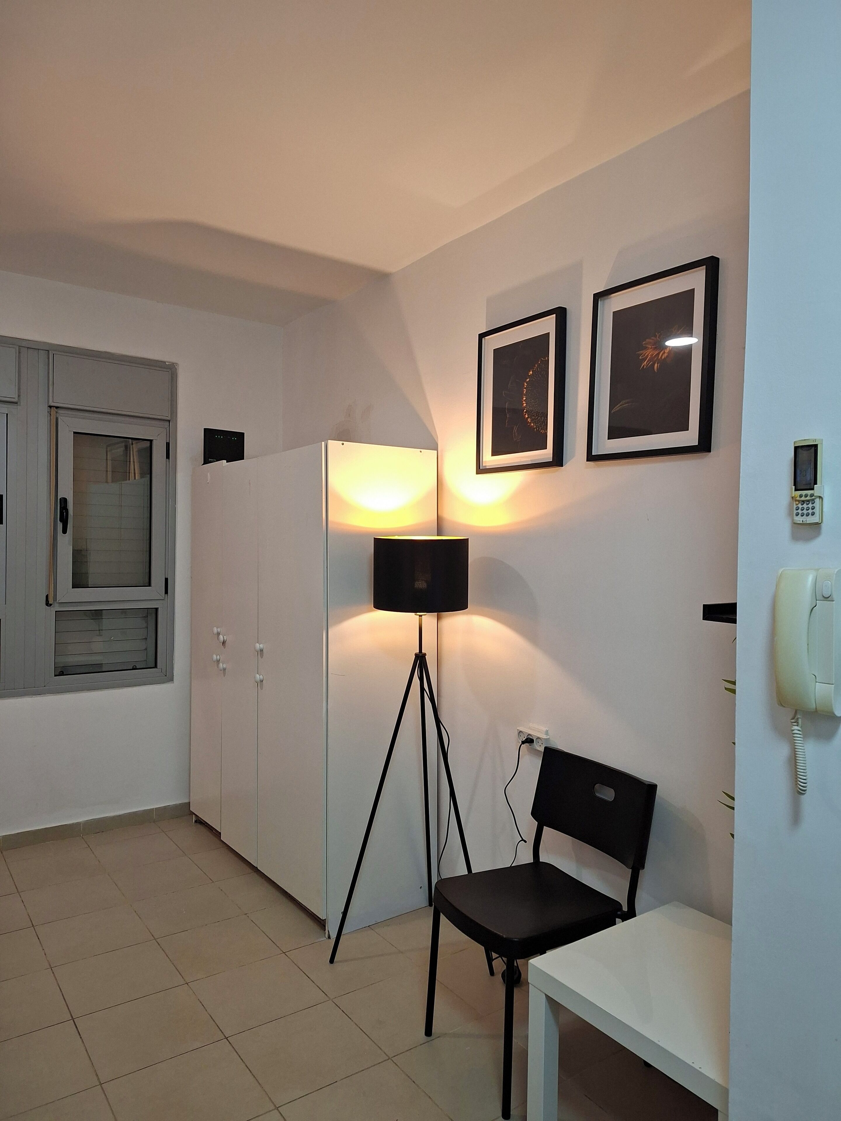 A room with a white cabinet, a floor lamp, a chair, and two framed pictures on the wall.