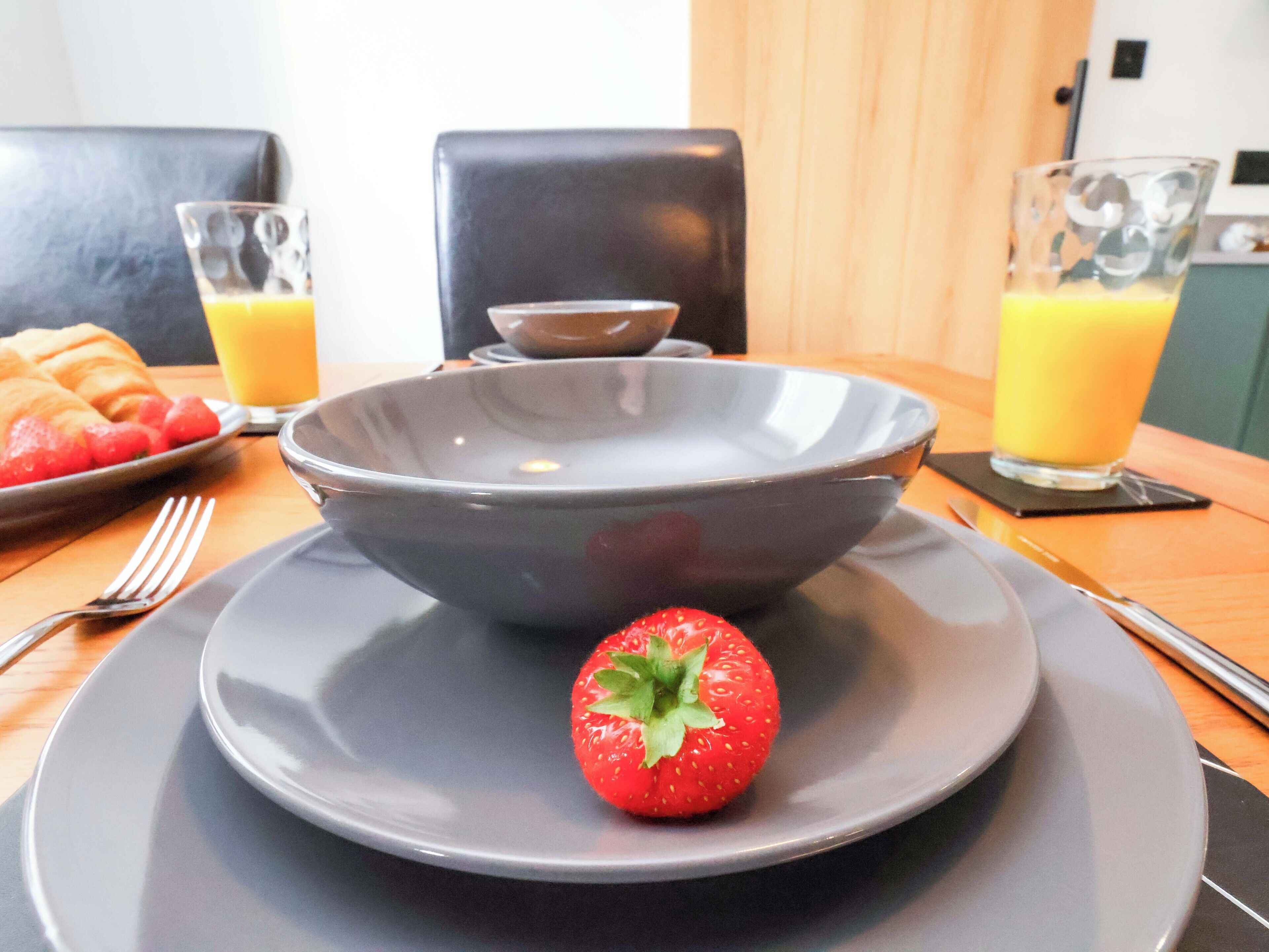 Morgenmadsbord med en skål, en tallerken med et jordbær, et croisant og glas med appelsinjuice.