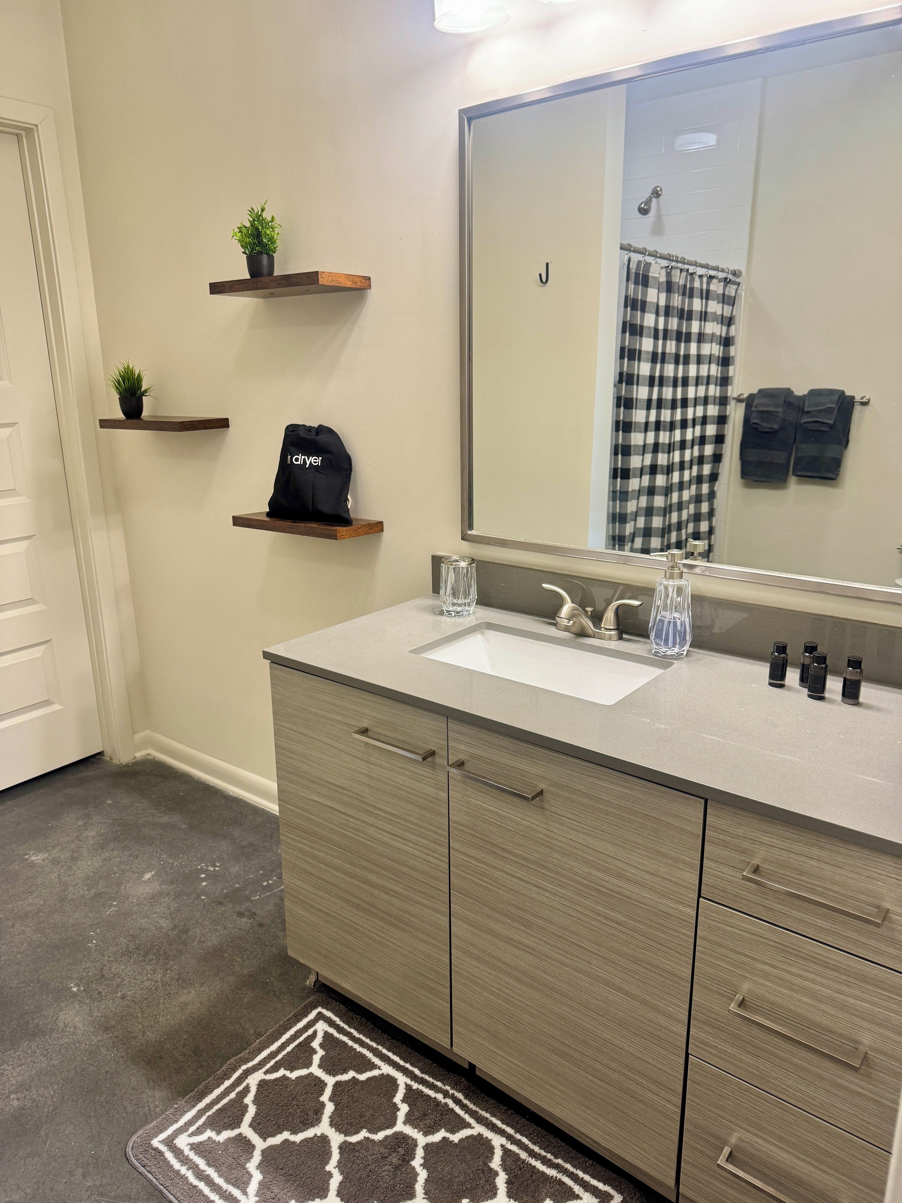 A modern bathroom with a large mirror, a sink, and a vanity with drawers. There are two small shelves with plants and a bag on one of them.