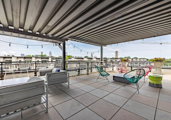 Une terrasse sur le toit, dotée d’un espace salon couvert, de chaises en métal et offrant une vue sur le paysage urbain.