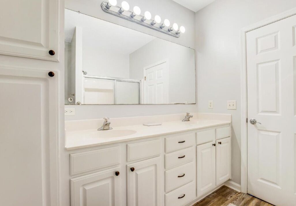Un baño con tocador blanco, un espejo grande con iluminación y una puerta.