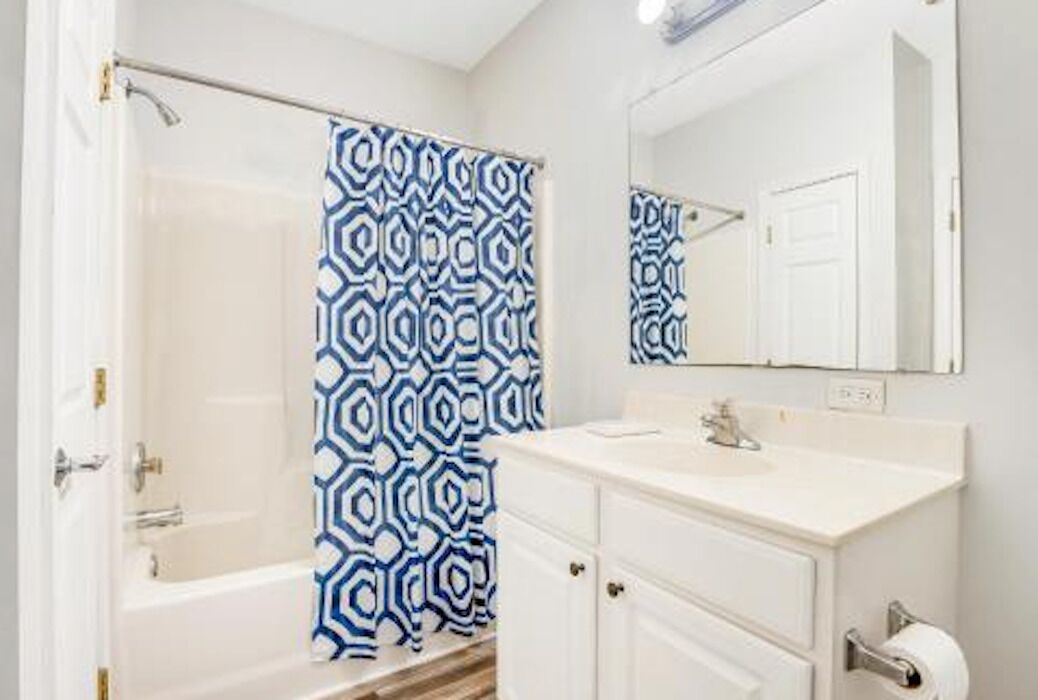 A bathroom with a white bathtub, a white vanity with a mirror, and a blue patterned shower curtain.