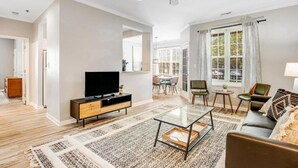 A modern living room with a flat-screen TV, a glass coffee table, a sofa, and a dining area in the background. - Rehoboth 2BR Condo Near Beach & Boardwalk (Rehoboth Beach)