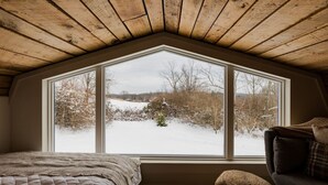 Un dormitorio acogedor en el ático con un ventanal grande, techo de madera y vistas a un paisaje nevado.