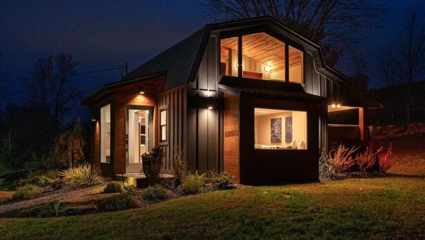 Una casa moderna con un amplio ventanal de vidrio, fachada de madera y una entrada bien iluminada.