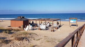 Een restaurant aan het strand met terras, een houten dek en uitzicht op de oceaan.