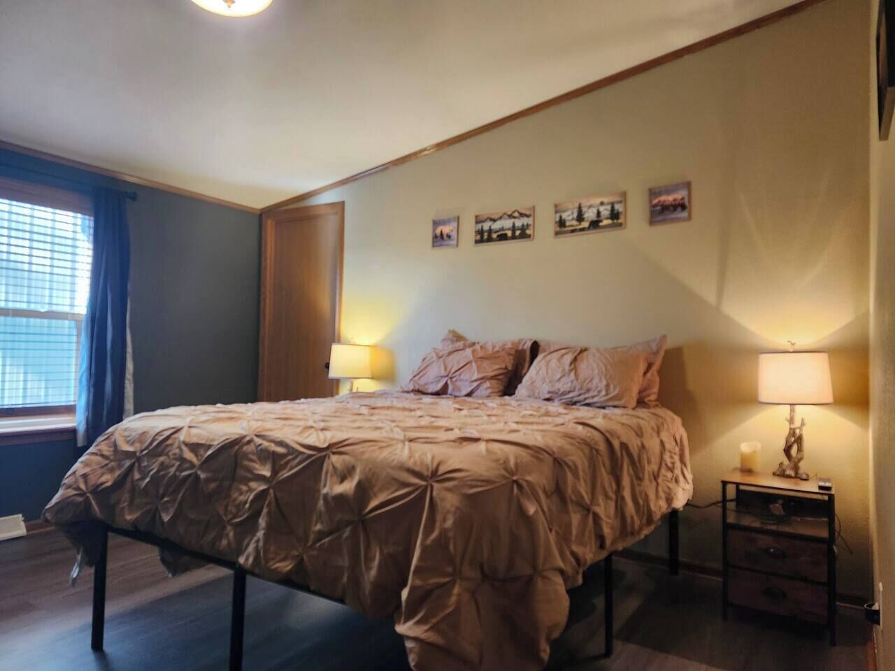 A bedroom with a large bed, a bedside table with a lamp, and a window with curtains.