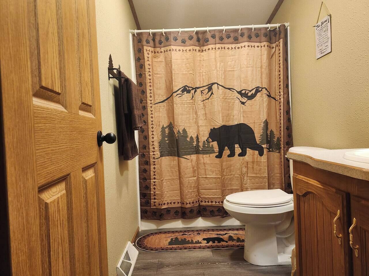 Een badkamer met een houten deur, een wit toilet en een douchegordijn met een ontwerp van een beer en bergen.