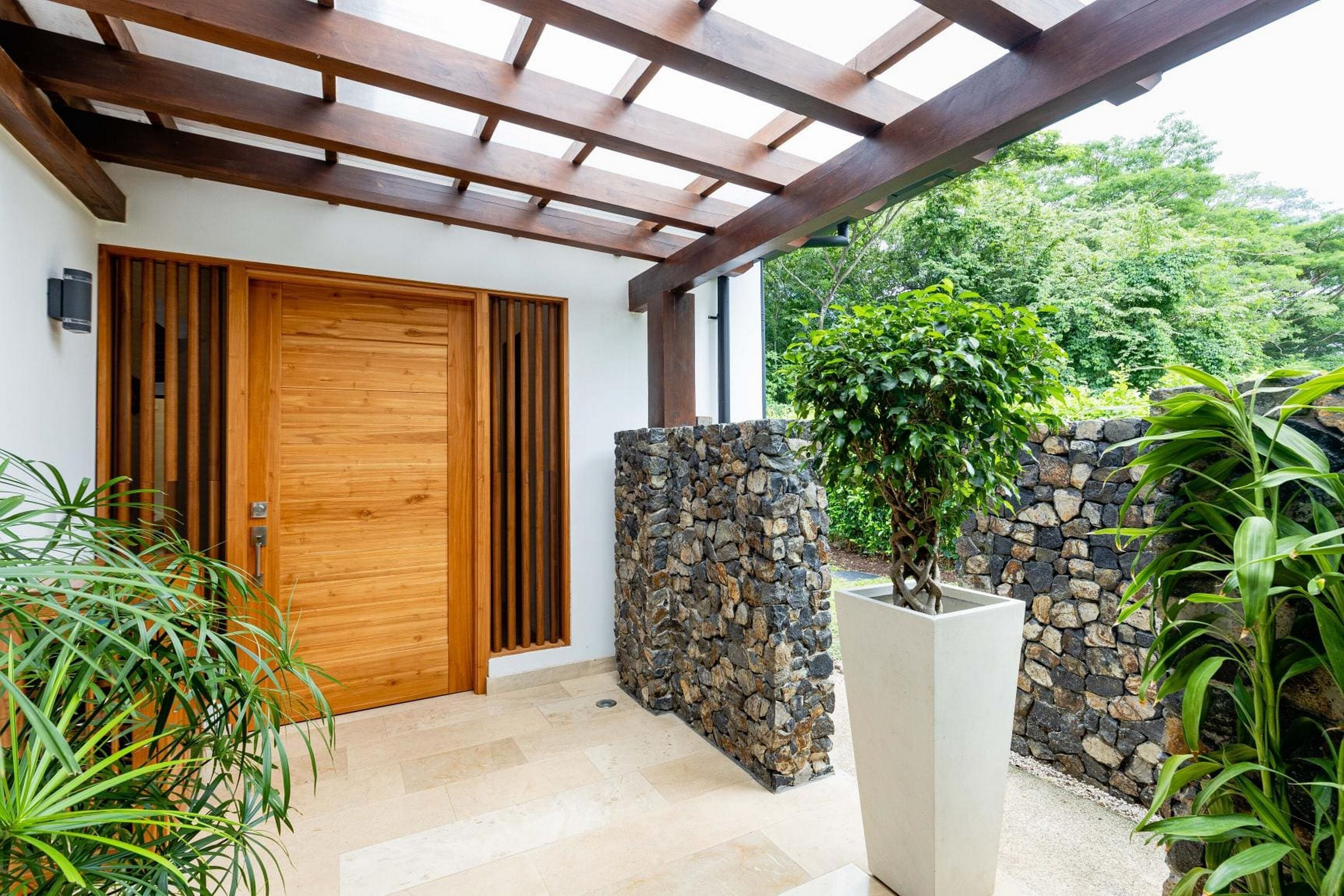 A wooden door with vertical slats, a stone wall, and a potted plant in a white planter.