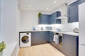 A modern kitchen with grey cabinets, a built-in washing machine, and a stainless steel oven. - Apt 2 Armatage Flats, Eyemouth (Eyemouth)