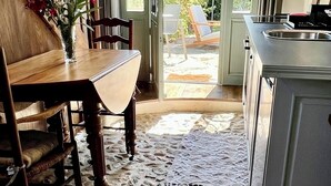A dining area with a wooden table and chairs, a vase with flowers, and a view of the outdoor patio through a glass door. - La Blanchie Haute, Gîte de charme d'exception pour 2 en Vallée de la Dordogne (Martel)
