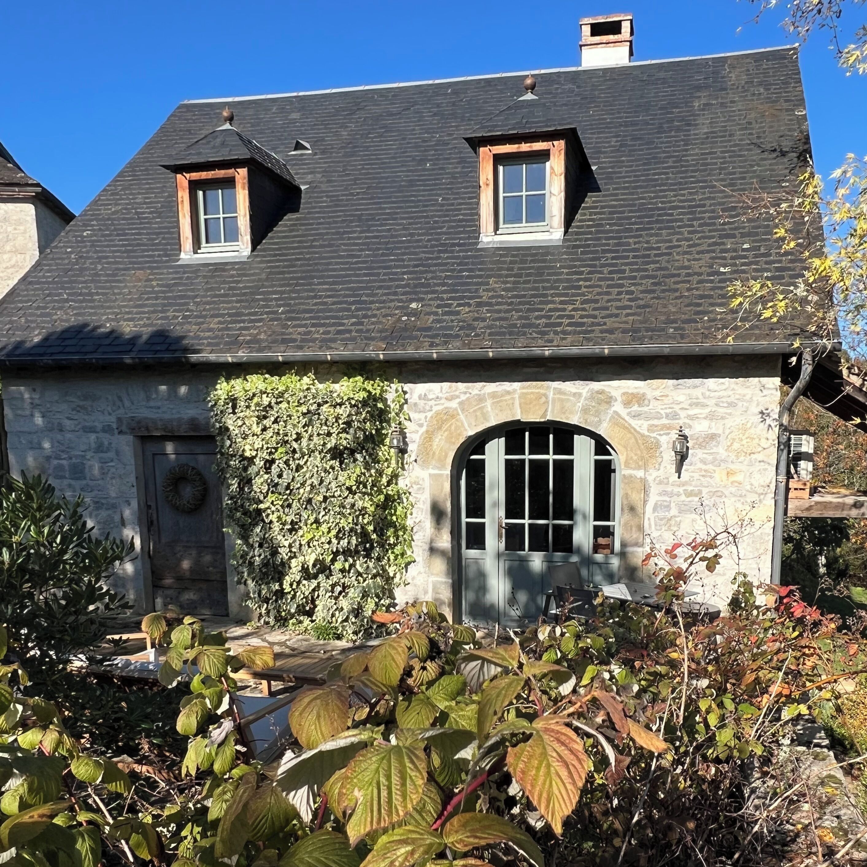Ein Steinhaus mit dunklem Dach, zwei kleinen Fenstern und einer steinernen Eingangstür.