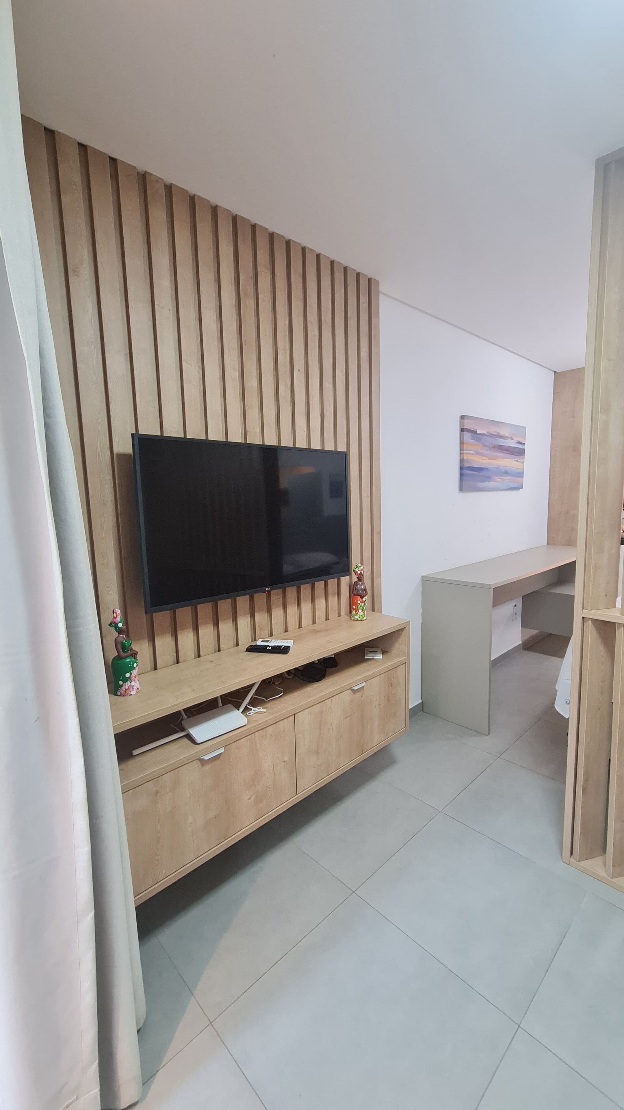 A modern living room with a flat-screen TV mounted on a wooden panel wall, a small cabinet with a remote control, and a decorative figurine.