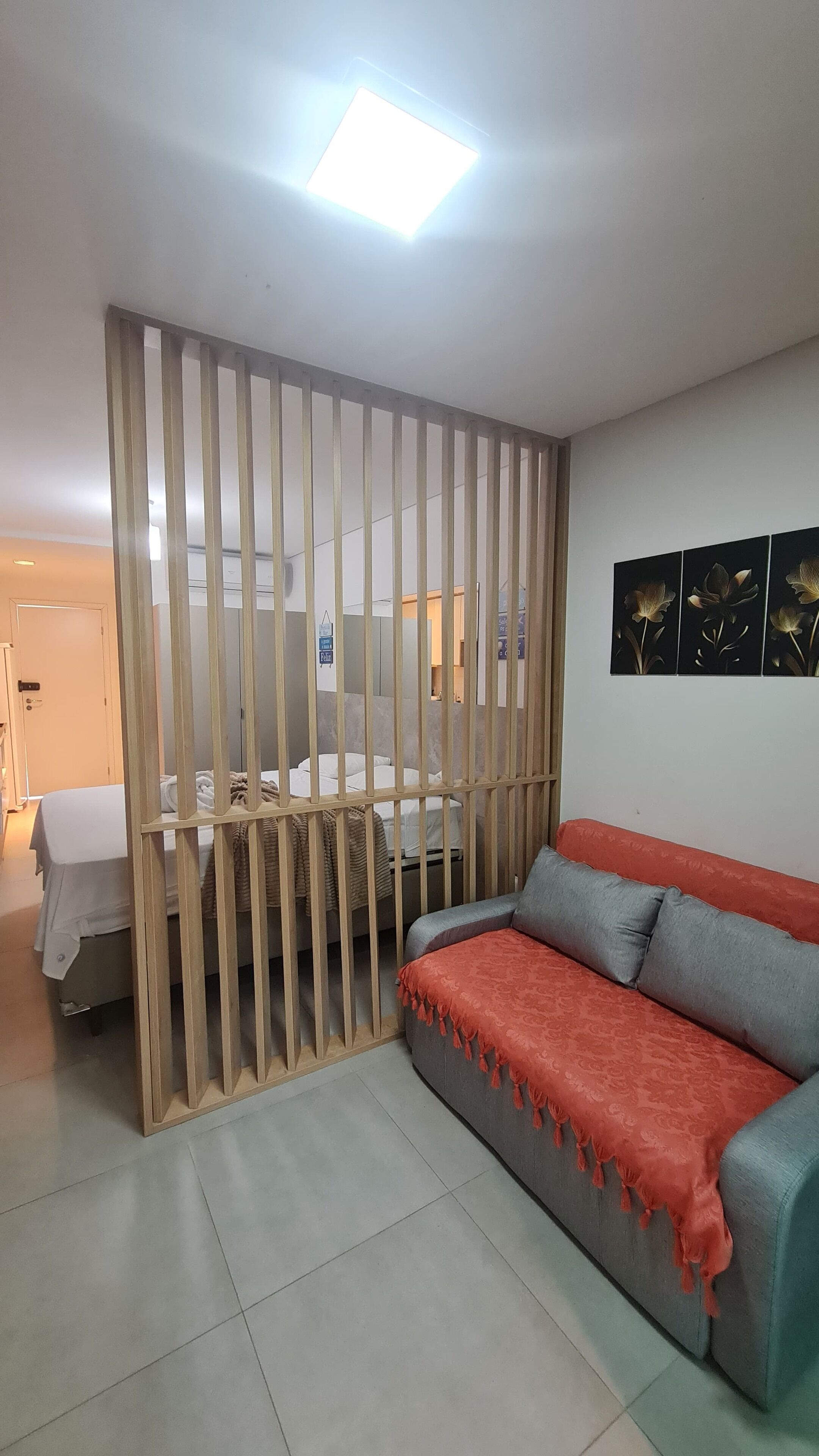 A room with a wooden partition, a grey sofa with a red throw, and a bed with white bedding.