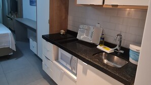 A compact hotel kitchen with white cabinets, a black countertop, a microwave, and a sink. - A 2  minutos do Mar  02PP by La Playa (Ipojuca)
