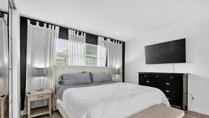Un dormitorio con cama, mesita de noche, banco, televisor y cómoda.