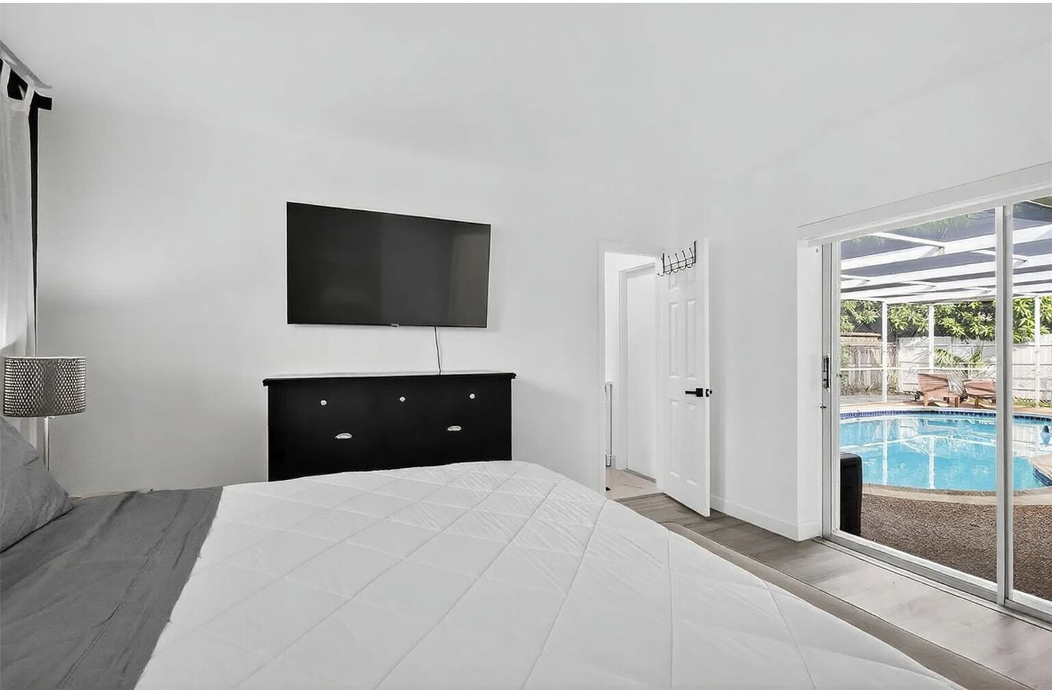 Un dormitorio con una cama, un televisor montado en la pared, un aparador y un ventanal corredera que da a una zona de piscina.