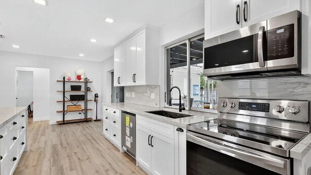 Una cocina moderna con armarios blancos, electrodomésticos de acero inoxidable y suelo de madera.