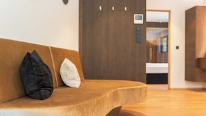 A modern interior with a curved sofa, a wooden door, and a glimpse of a bathroom. - Holiday Apartment ‘Erbacher – Gabi’s Suite’ with Mountain View, Sauna and Pool (Bozen)