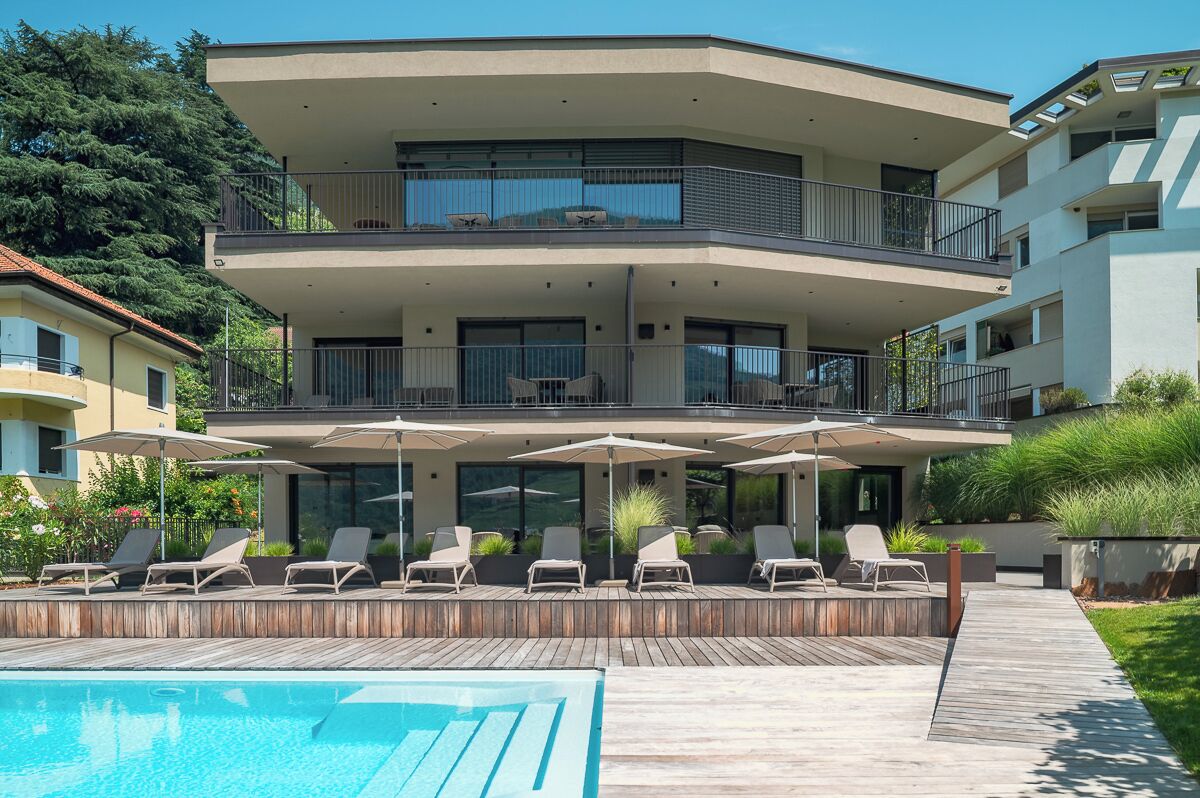 Ein modernes Mehrstöckige Gebäude mit Poolbereich auf dem Dach, Sitzgelegenheiten im Freien und einem gepflegten Garten.