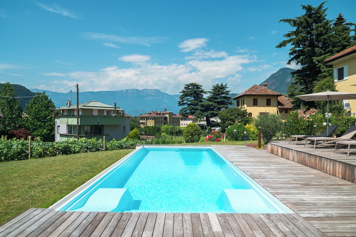 Una piscina rectangular con muelle de madera, rodeada de abundante vegetación y edificios residenciales.
