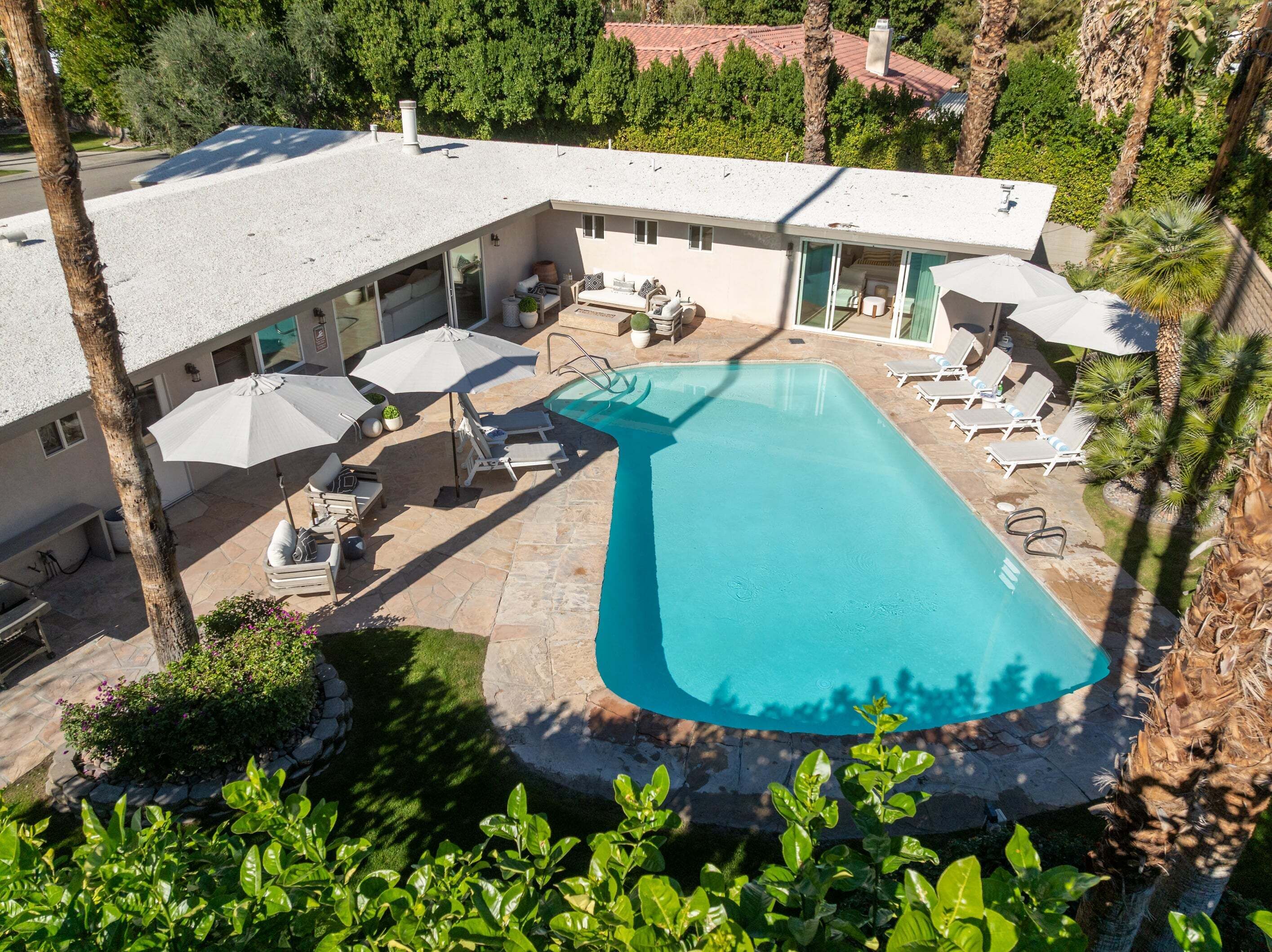 Una casa moderna con piscina, mobiliario exterior y vistas a la vegetación circundante.