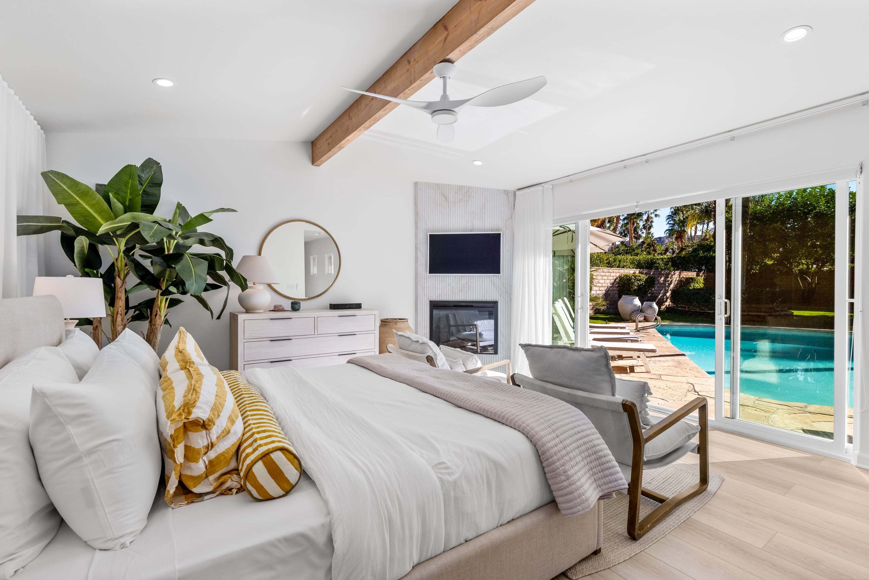 A bedroom with a bed, a TV, a ceiling fan, and a view of a swimming pool.