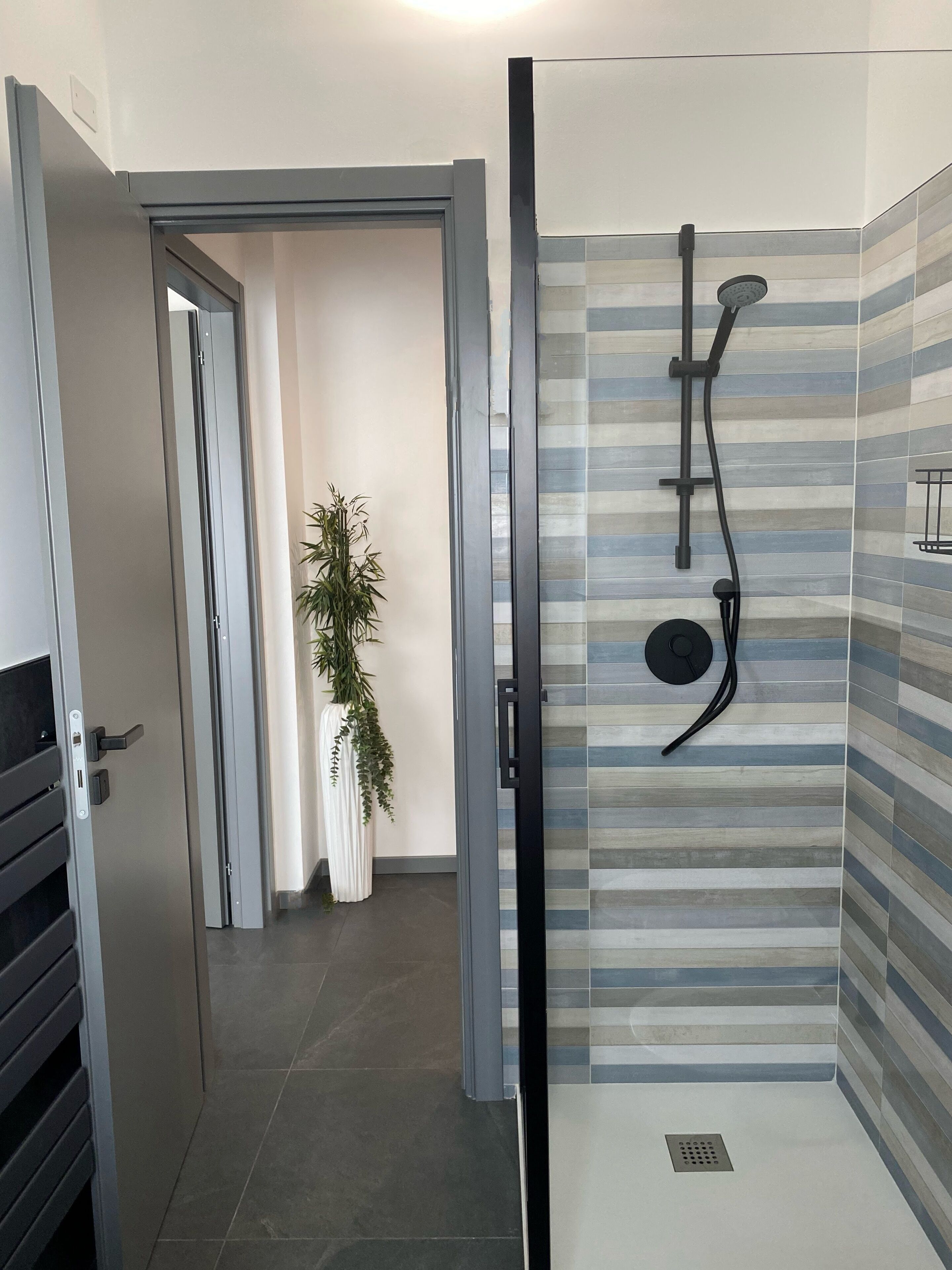 Un bagno moderno con doccia, piastrelle a righe e una pianta in vaso.