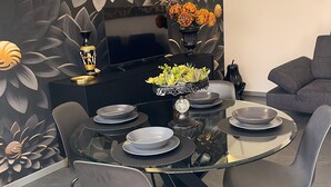 Et moderne spiseområde med et glasbord, sorte stole og et sort konsolbord med et fladskærms-tv.