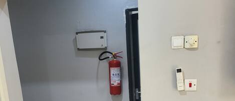 A hallway with a fire extinguisher, a thermostat, and a light switch on the wall.