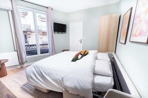 A bedroom with a bed, a television on the wall, and a window with a view of buildings. - Gare de Lyon - charming modern studio (Paris)