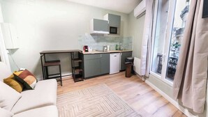 A compact living space with a kitchenette, a sofa, and a view through a large window. - Gare de Lyon - charming modern studio (Paris)