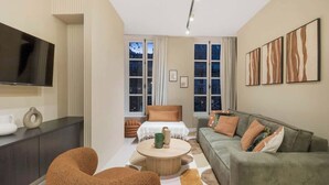 A modern living room with a sofa, armchair, and a coffee table. There is a television mounted on the wall, and a window with curtains. - Élégant 3 pièces climatisé au cœur du Marais (Paris)