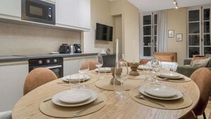 A modern kitchen with a microwave, stove, and coffee maker. There is a dining table set with plates, glasses, and cutlery. - Élégant 3 pièces climatisé au cœur du Marais (Paris)