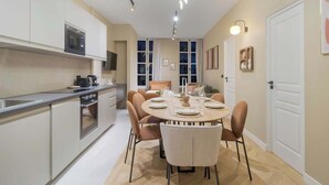 A modern kitchen with a dining area, featuring a built-in oven, microwave, and a dining table set for four. - Élégant 3 pièces climatisé au cœur du Marais (Paris)