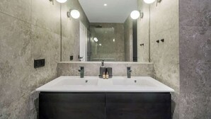 A modern bathroom with a large mirror, two sinks, and wall-mounted lighting. - Élégant 3 pièces climatis é au cœur du Marais (Paris)