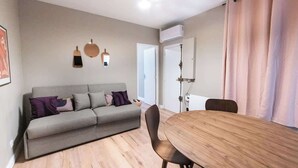 Een moderne woonkamer met een grijze bank, een houten eettafel en een lichtgekleurde vloer.