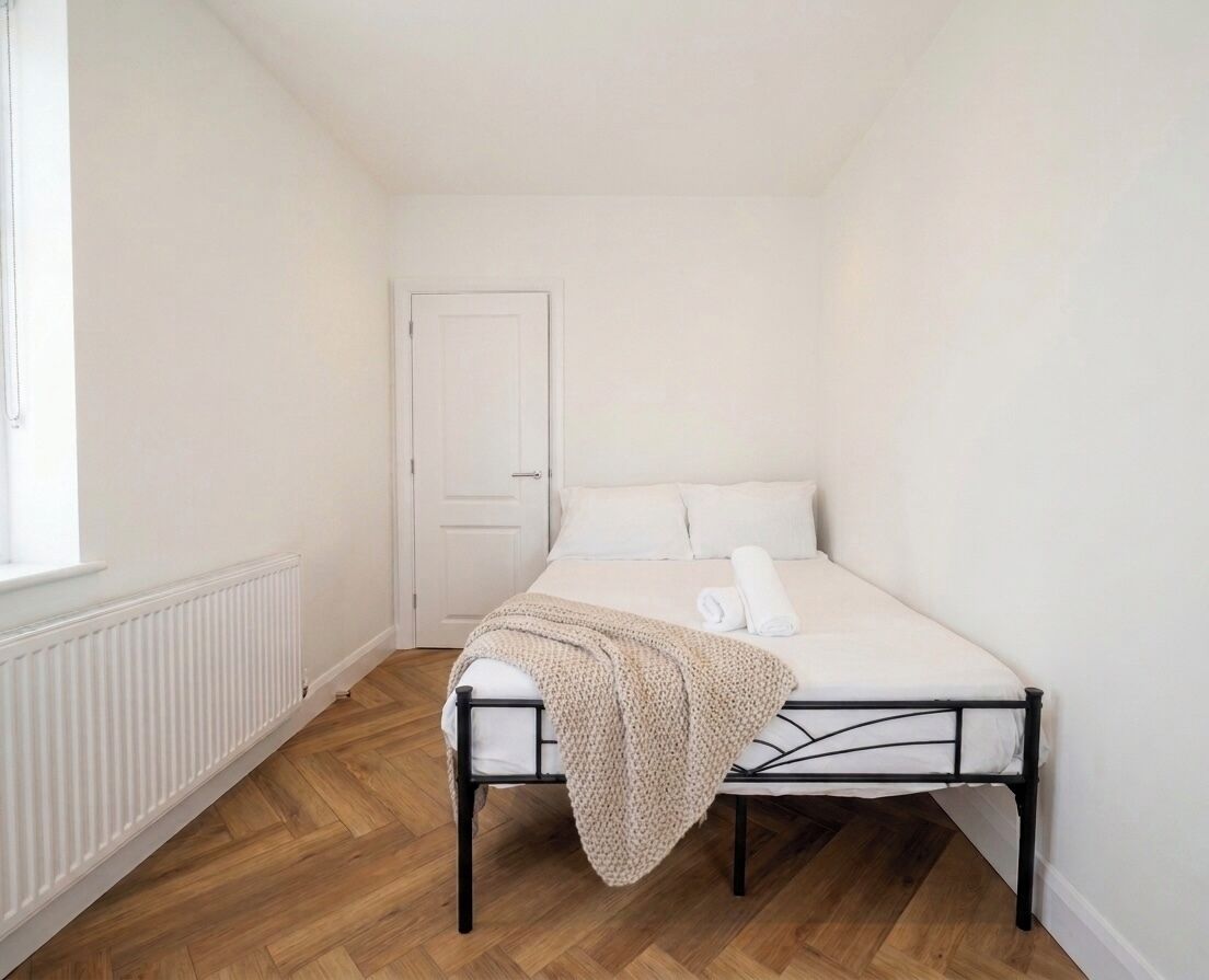 A bedroom with a bed, a radiator, a door, and a window.