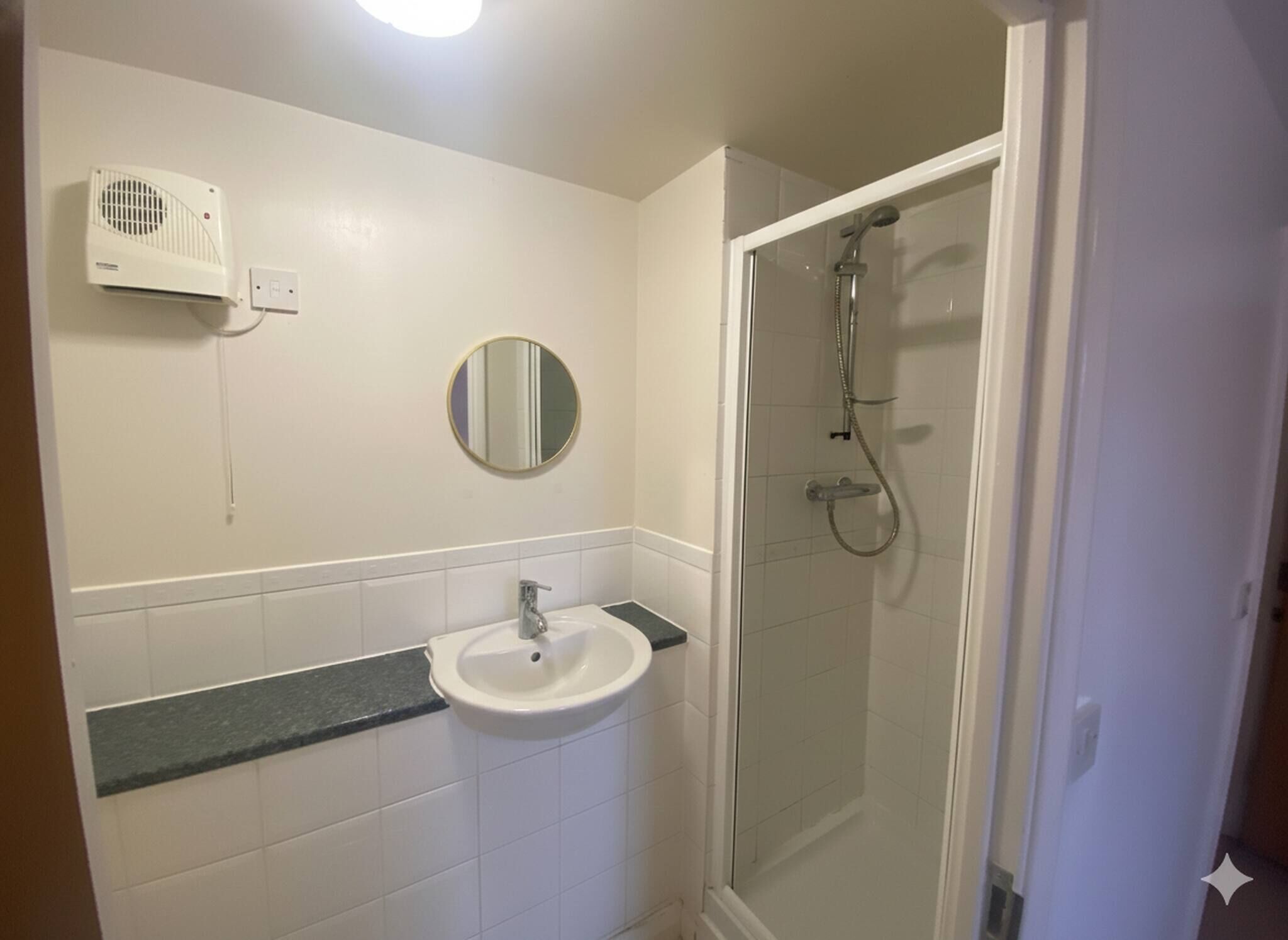 A bathroom with a white sink, a mirror, a shower enclosure, and a ceiling fan.